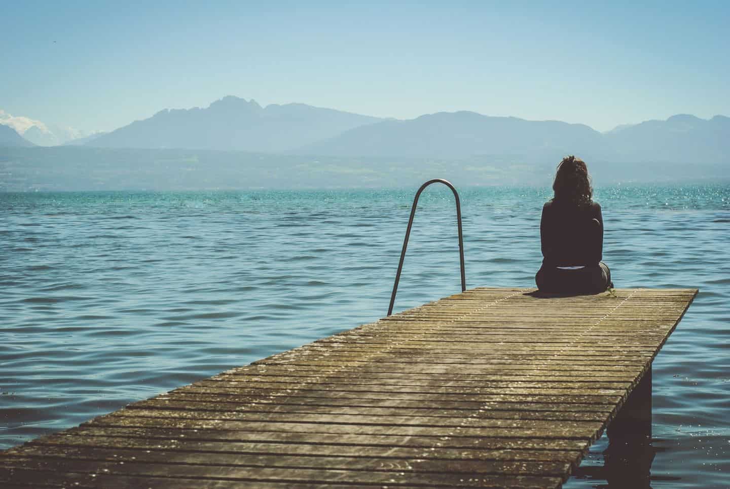 Frau sitzt auf dem Steg an einem See, der in der Sonne blau schimmert