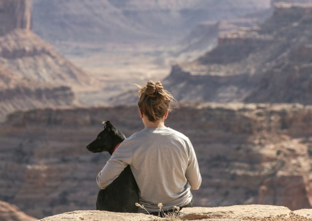 Frau mit Hund sitzt am Rande eines Canyons