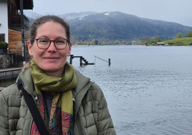 Evelyn mit Winterjacke vor dem Tegernsee und Bergen im Hintergrund